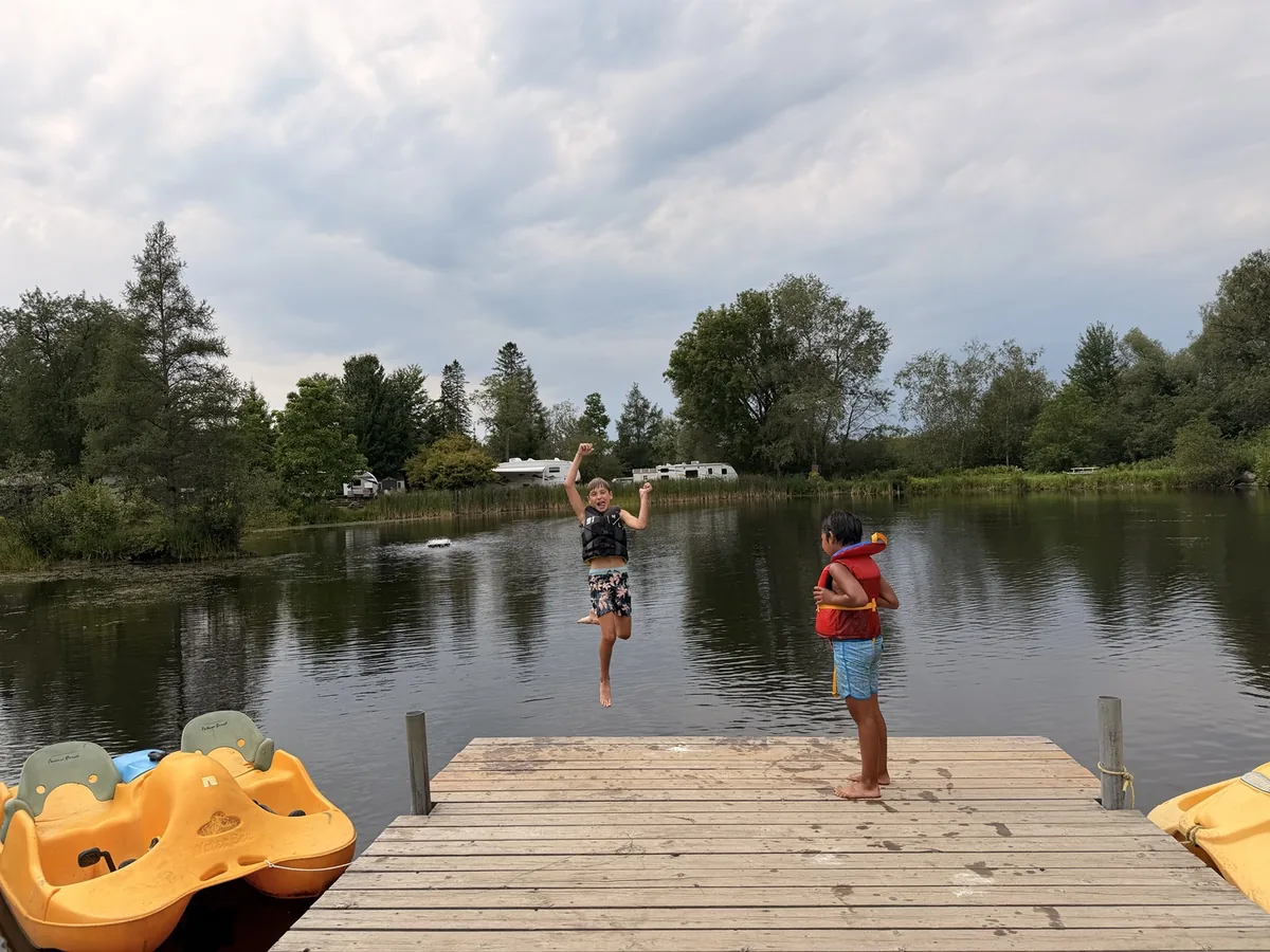 Enfant avec gilet de flottaison sautant du quai dans le petit lac du camping