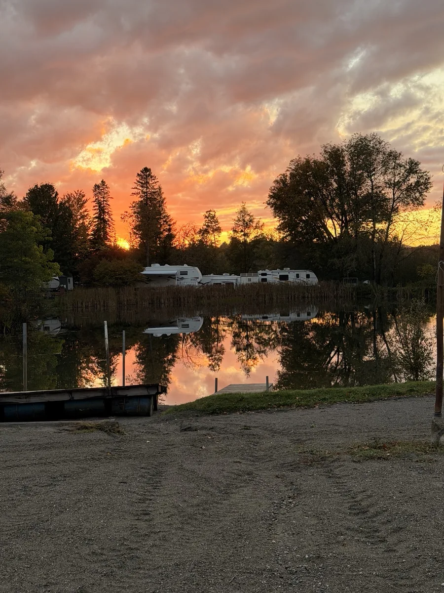 Nuages orangés et arbres reflétés dans le petit lac du camping